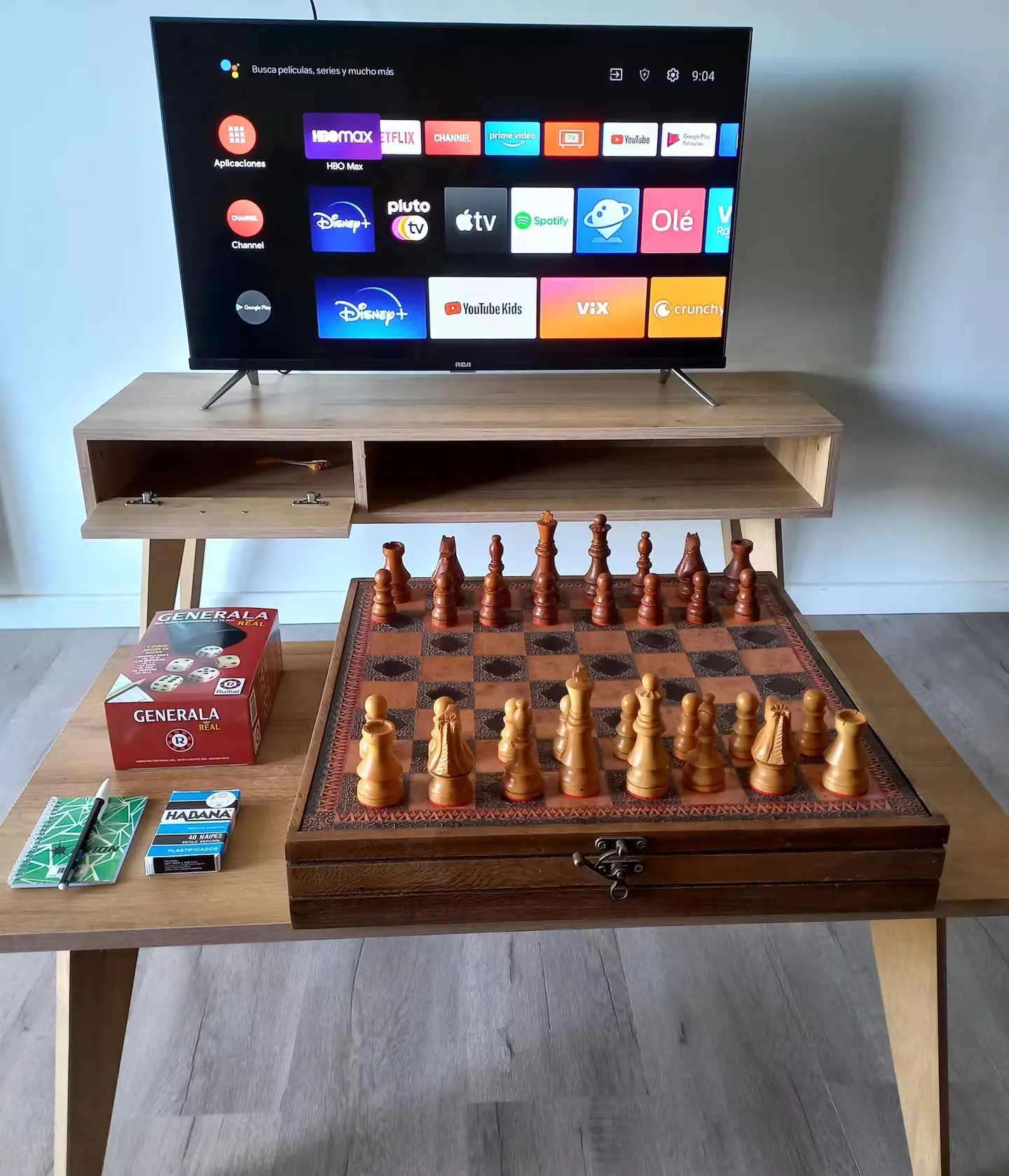 Mesa con ajedrez, generala y naipes junto al televisor smart