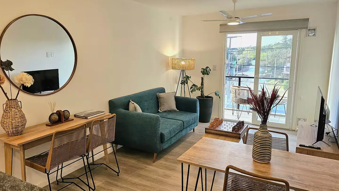Living del departamento con puerta corrediza abierta al balcón, con la pileta del complejo de fondo